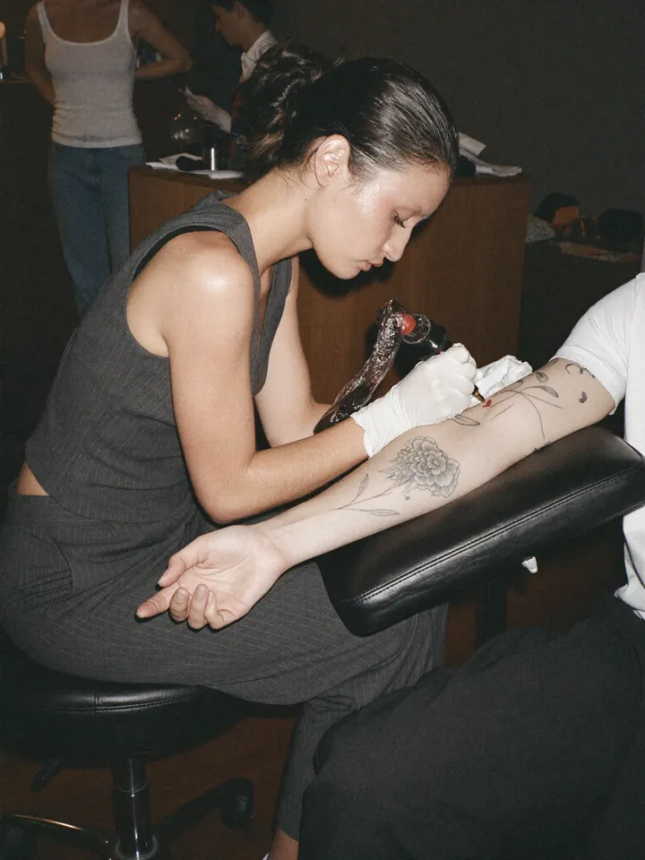 A tattoo artist working on a fine-line floral tattoo